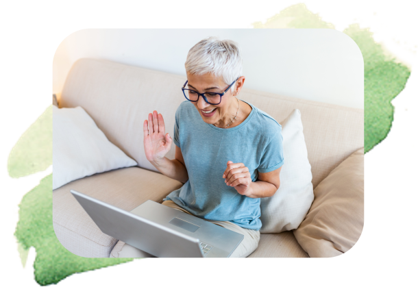 Ältere Frau sitzt mit Laptop auf dem Schoß auf einer Couch und freut sich